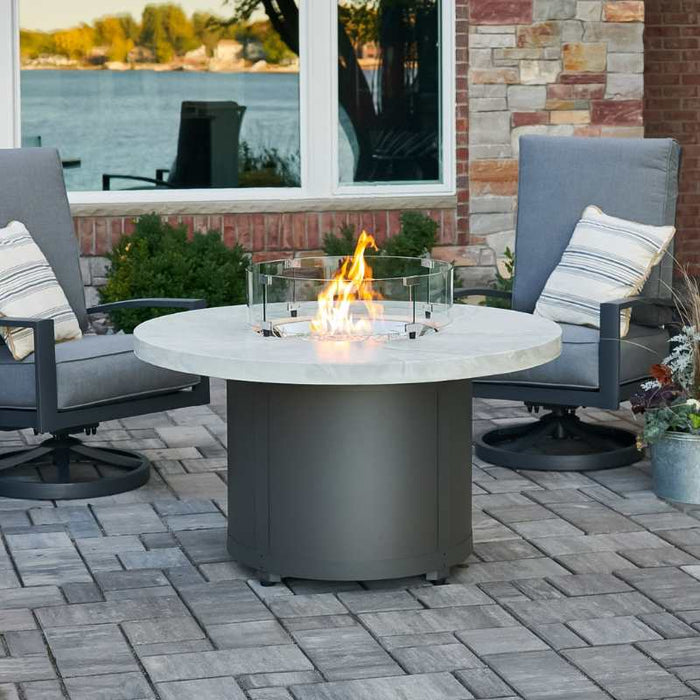 Beacon 48 Round Gas Fire Pit Table White Onyx Place at the Front Yard with Clear Tempered Fire Glass Gems plus Fire Burner On and Glass Wind Guard