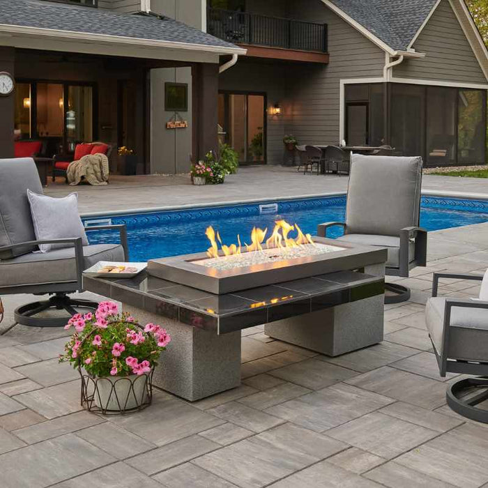 The Outdoor Greatroom Black Uptown Linear Gas Fire Pit Table Installed Near Pool with Clear Tempered Fire Glass Gems and Glass plus Fire Burner On