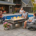 The Outdoor Greatroom Black Uptown Linear Gas Fire Pit Table Installed Near Pool with Family with Clear Tempered Fire Glass Gems and Glass plus Fire Burner On and Glass Wind Guard Installed