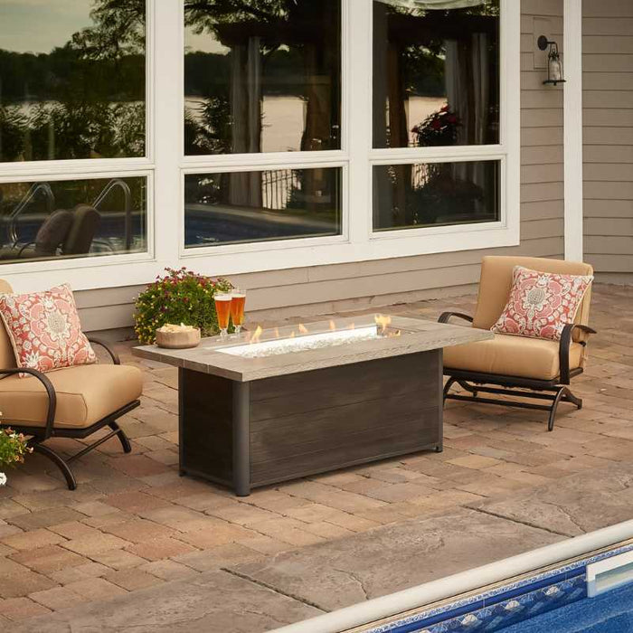 The Outdoor Greatroom Cedar Ridge Linear Gas Fire Pit Table near Pool with Clear Tempered Fire Glass Gems and Fire Burner On